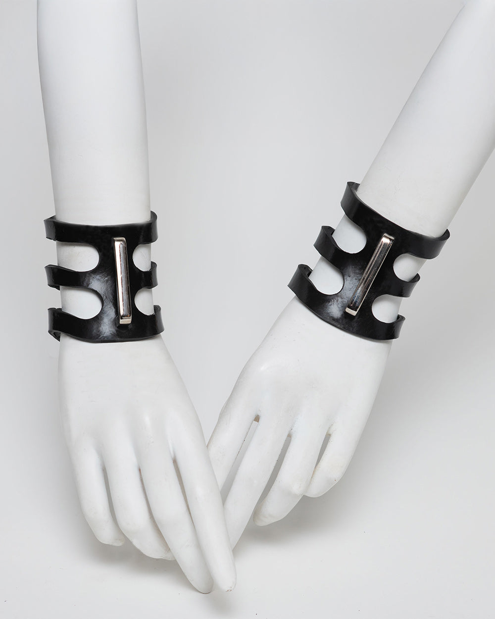 Black rubber cuffs on white mannequin hands against a white background
