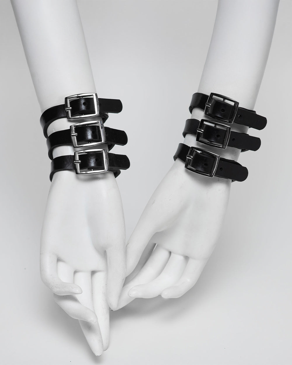Black rubber bracelets with buckles on white mannequin hands against a light gray background