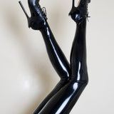 A models legs are shown wearing the black latex thigh high stockings against a tan background. 