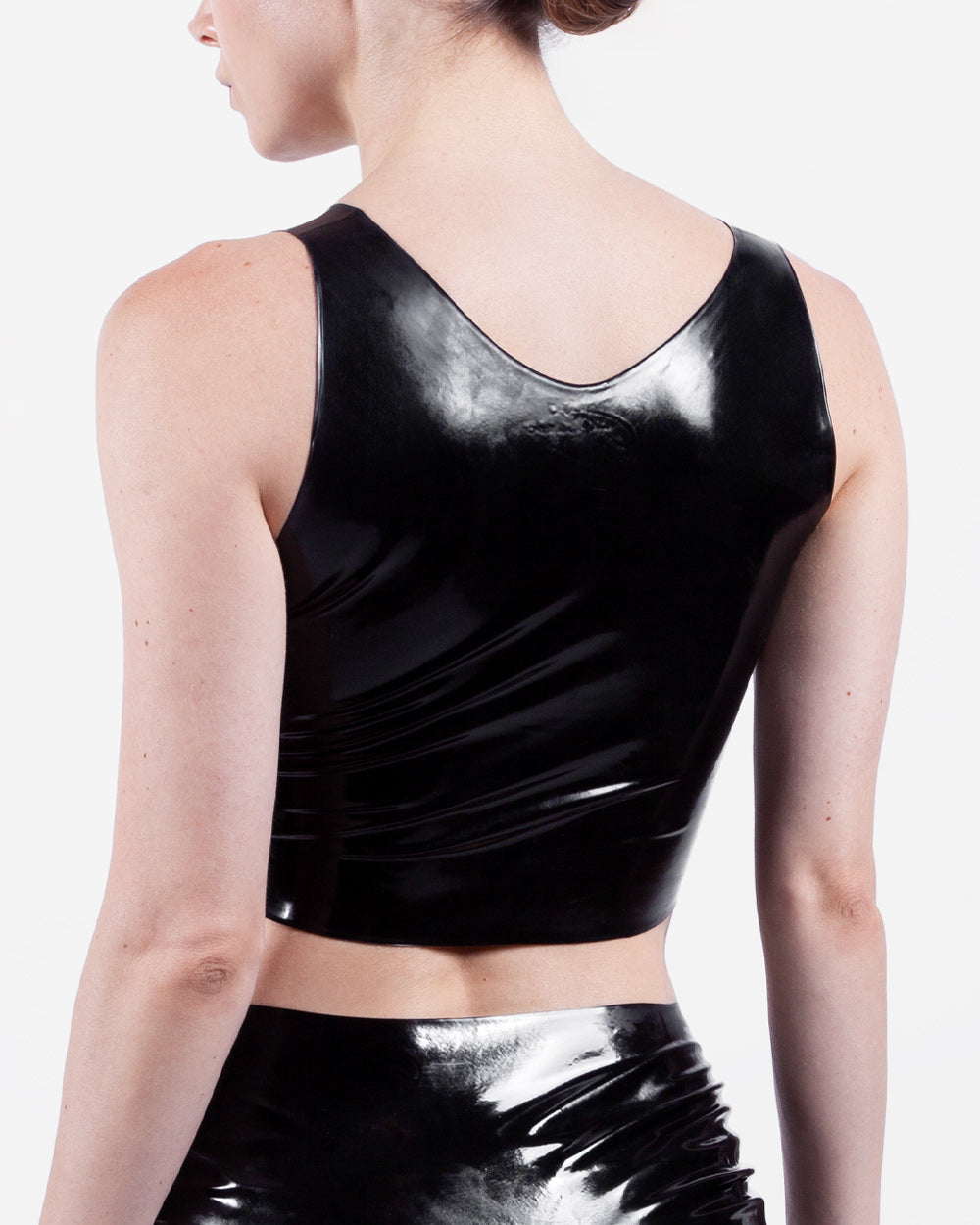 The back of a person wearing a black latex crop top on a white background