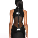 A close-up of a model is shown from the back wearing the black casey latex dress standing in front of a white 