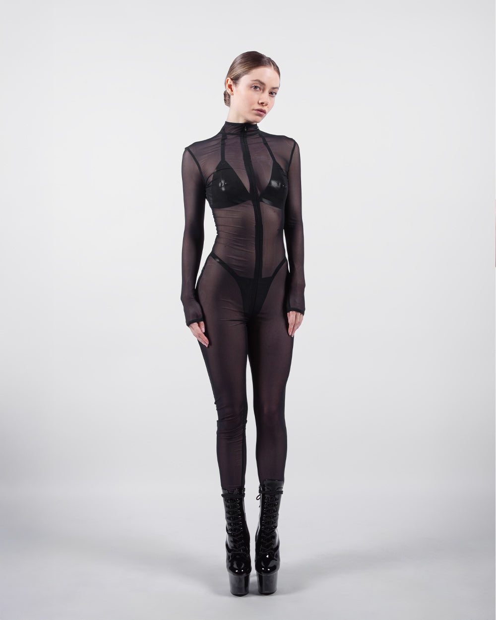 Model wearing a black bodysuit with sheer panels on a white background