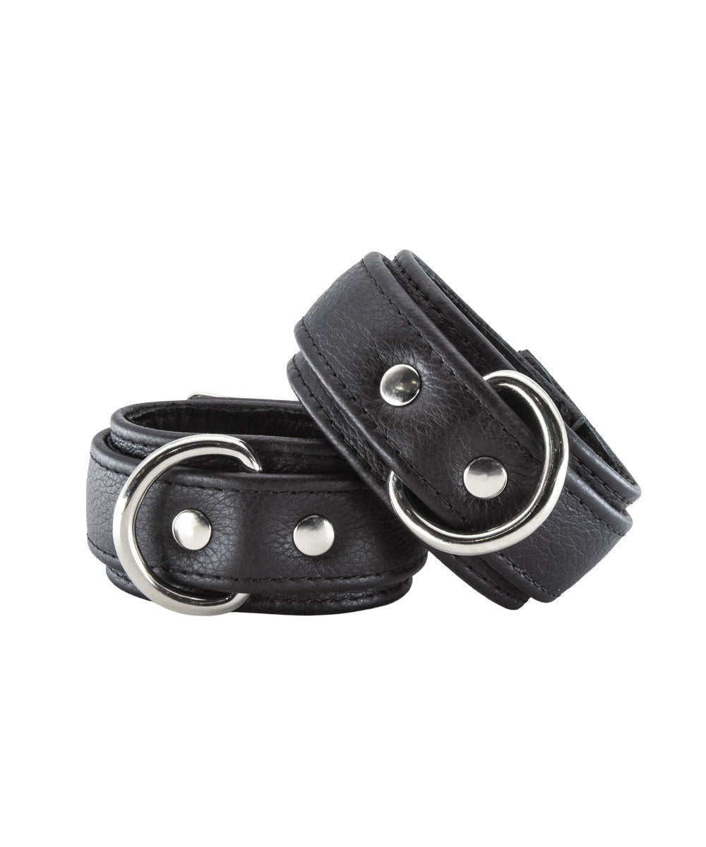 A pair of Premium Garment Leather Wrist Cuffs in black are shown against a blank background. The cuffs are made of black leather with silver hardware. They each have a D-ring and a lockable metal buckle.