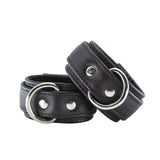 A pair of Premium Garment Leather Wrist Cuffs in black are shown against a blank background. The cuffs are made of black leather with silver hardware. They each have a D-ring and a lockable metal buckle.