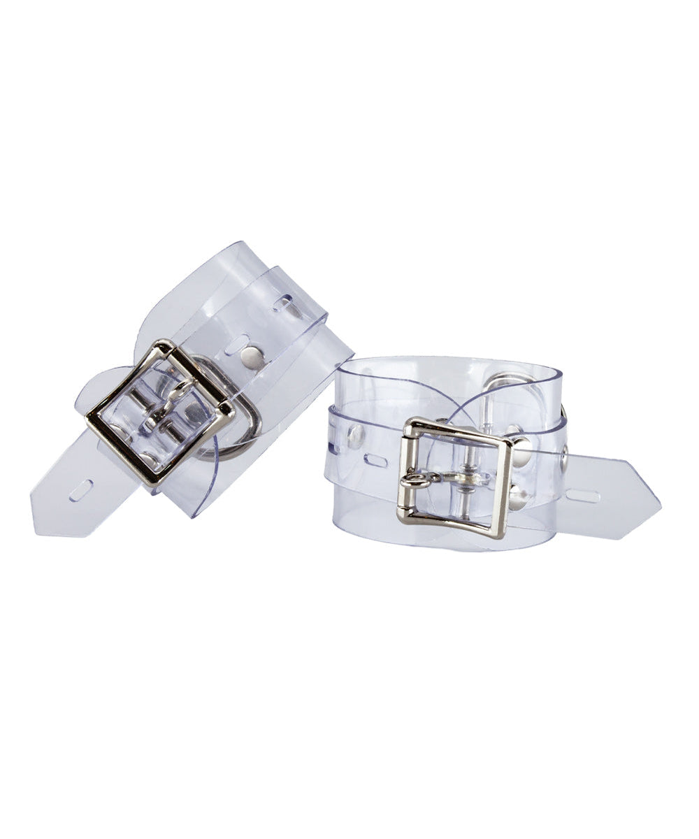 The Clear CTRL Clear Vinyl Wrist Cuffs are shown from the back against a blank background. The cuffs are completely transparent with metal hardware. They each have a lockable buckle with an adjustable strap and a D-ring.