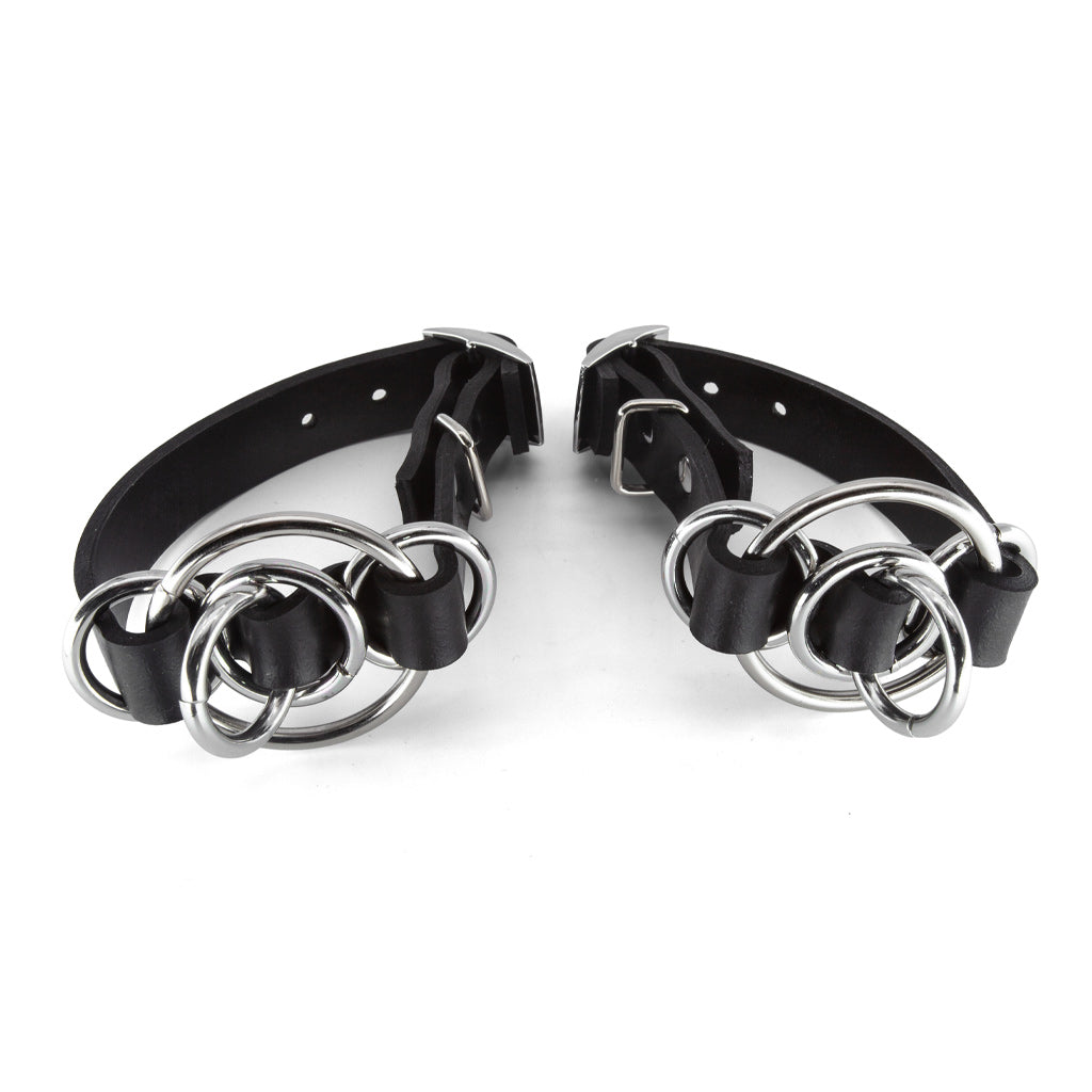 Pair of black leather cuffs with silver metal rings on a white background