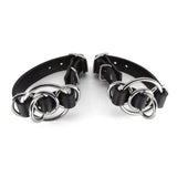 Pair of black leather cuffs with silver metal rings on a white background