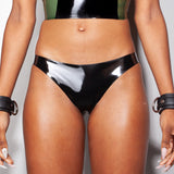 A close-up of a models waist is shown wearing the Syren latex mila panty in black. She is standing in front of a light gray background. 
