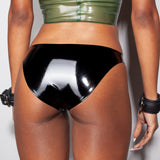 A close-up of a models waist is shown wearing the Syren latex mila panty in black. She is standing in front of a light gray background. 