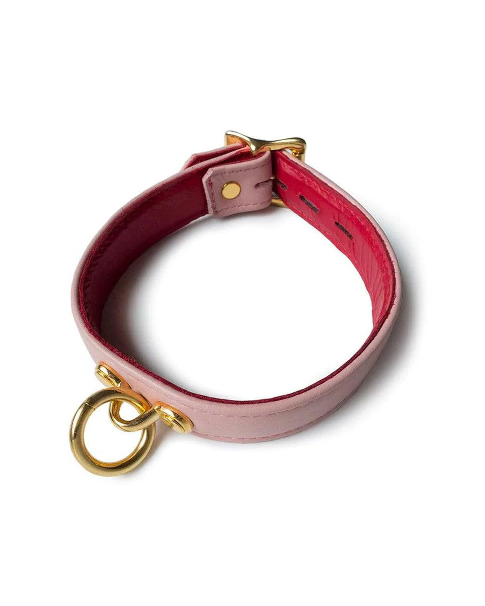 The Premium Garment Leather Collar With 18k Gold Plated Hardware is displayed against a blank background. The collar is made of light pink leather with a red lining. The collar has a dangling O-ring at the front and a buckle in the back.