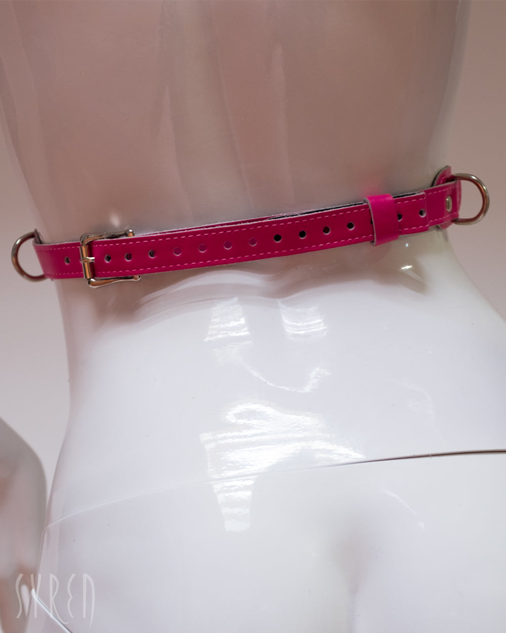 The waist buckle of the  neon angel pink leather bust harness is shown on a mannequin in front of a white background.