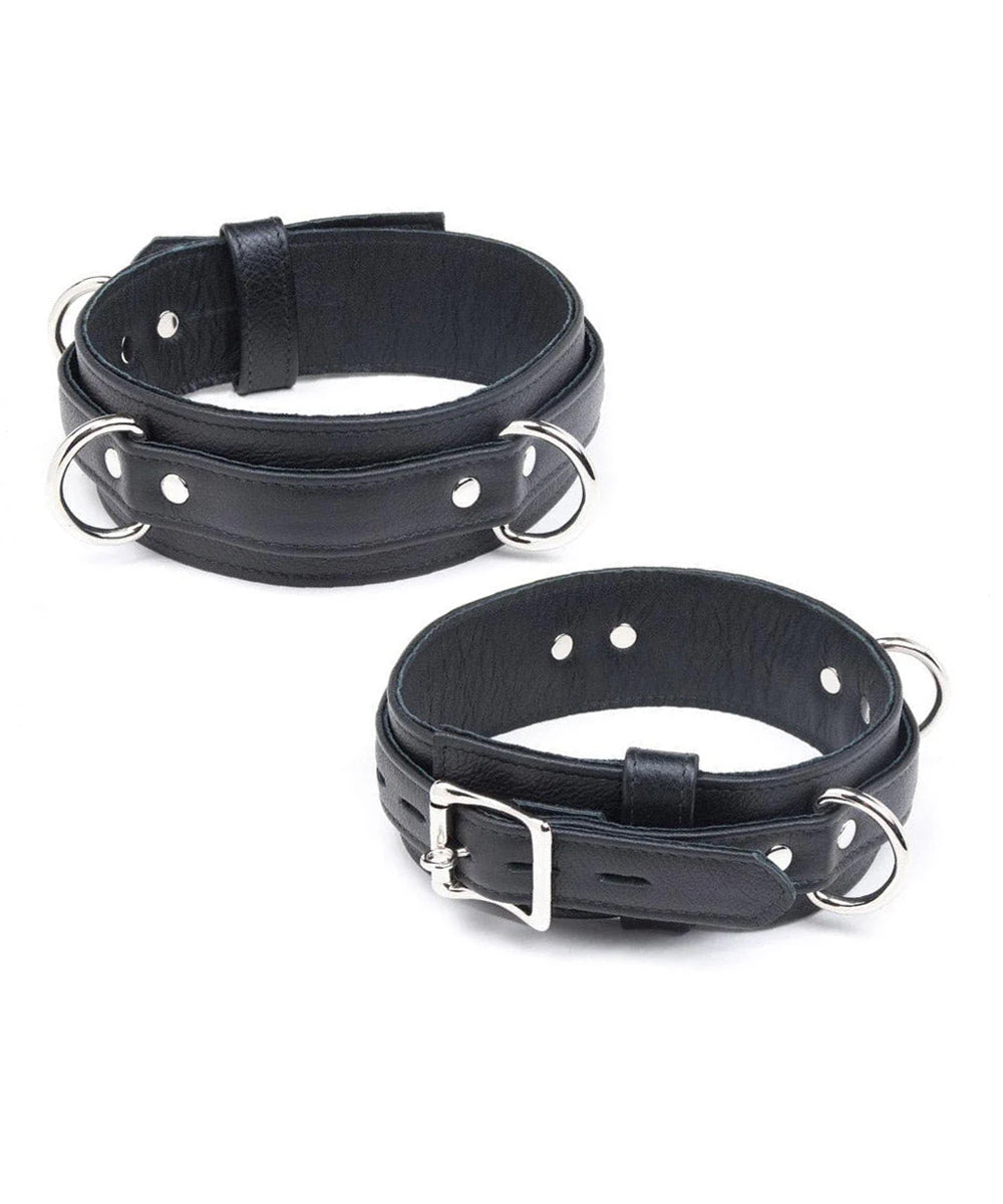The Premium Garment Leather Locking Thigh Restraint set in black is displayed against a blank background. It is a thick band of black leather with silver metal hardware. The cuff has three evenly spaced D-rings.