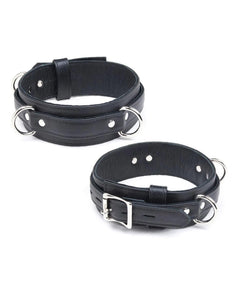 The Premium Garment Leather Locking Thigh Restraint set in black is displayed against a blank background. It is a thick band of black leather with silver metal hardware. The cuff has three evenly spaced D-rings.