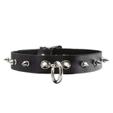 The Leather Collar with Spikes is shown against a blank background. It is made of black leather with metal hardware. There are spikes projecting outwards around the collar and a dangling O-ring in the front.