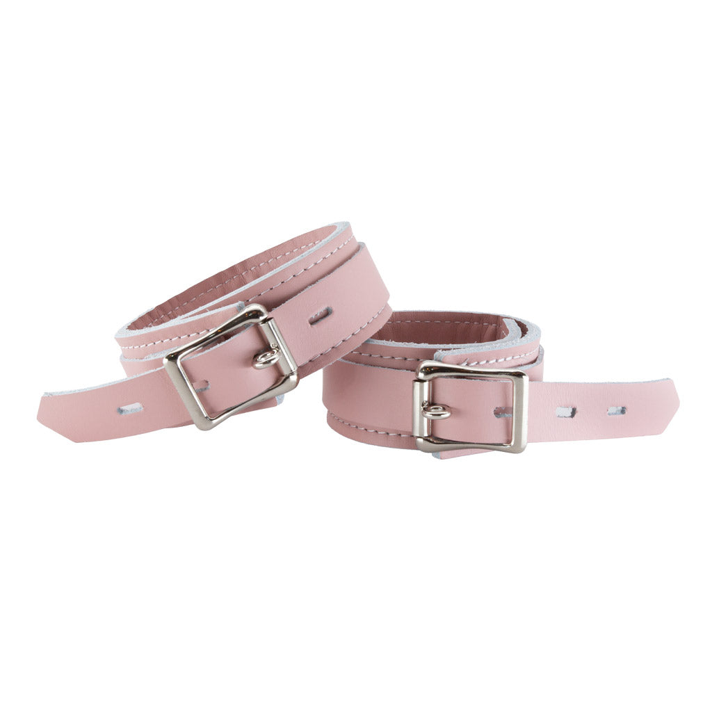The Stupid Cute Wrist Cuffs are shown from the back fastened against a blank background. The leather is pink with white edges and white stitching on the borders. They have a silver D-Ring and fasten with a lockable buckle.