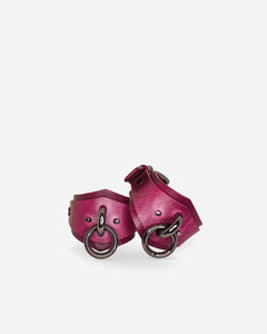 Pair of pink leather cuffs with metal rings on a white background