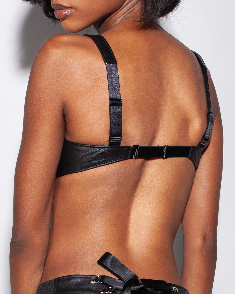 Black leather bra worn by a person on a plain background