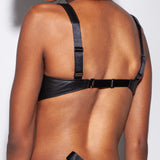 Black leather bra worn by a person on a plain background